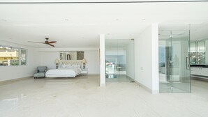 A spacious bedroom with a large bed, a ceiling fan, and a view through a glass door to a balcony.