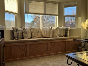 Une pièce avec une banquette intégrée le long d’une fenêtre, un meuble en bois et une table avec un plateau en verre.