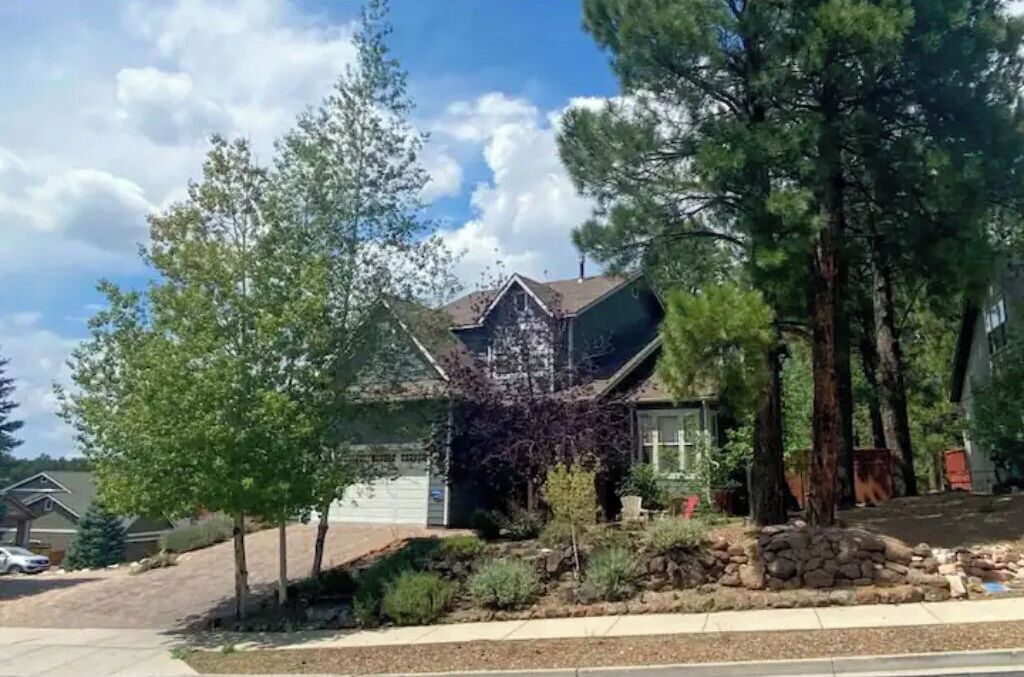 A residential house with a sloped roof, surrounded by trees and a stone wall.