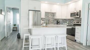 A modern kitchen with white cabinets, a central island with bar stools, stainless steel appliances, and a stone backsplash.