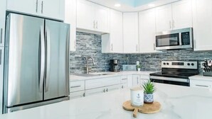 Una cocina moderna con gabinetes blancos, un refrigerador de acero inoxidable, un microondas y una estufa.