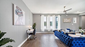 A modern living room with a blue sofa, a dining area with a table and chairs, and a ceiling fan. - Your lavish contemporary duplex | downtown Houston| Rooftop. (Houston)