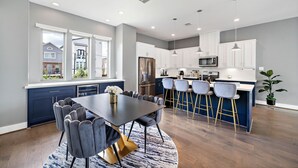 A modern kitchen with white cabinets, a central island with bar stools, and a dining area with a large table and chairs. - Your lavish contemporary duplex | downtown Houston| Rooftop. (Houston)