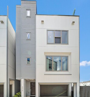 Uma casa moderna de dois andares com garagem, uma pequena varanda e uma chaminé.