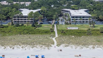 A hotel with multiple buildings, a parking lot, and a beach area with umbrellas.