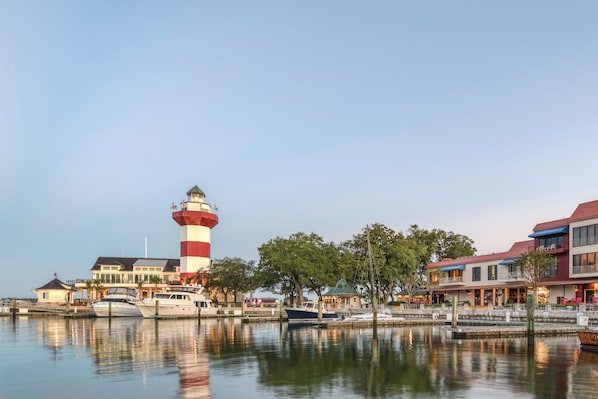 A waterfront property with a prominent lighthouse, docked boats, and a row of buildings with balconies.