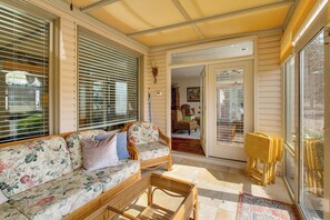 A sunlit room with a sofa, wicker chairs, and a glass door leading to another room.