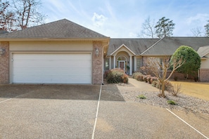 A two-story house with a garage, a driveway, and a landscaped front yard with shrubs and a tree.