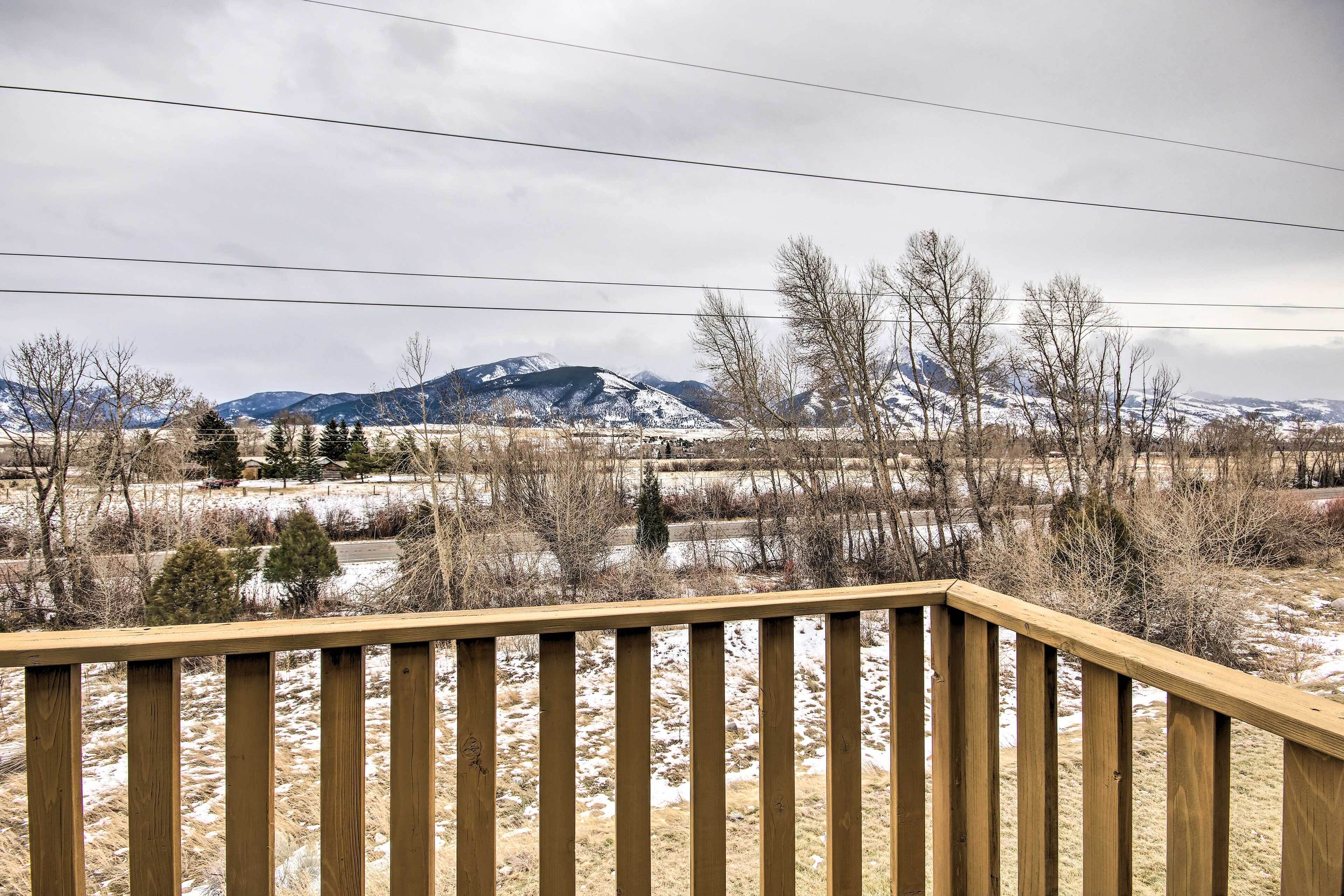 A wooden deck overlooking a snowy landscape with mountains in the background.