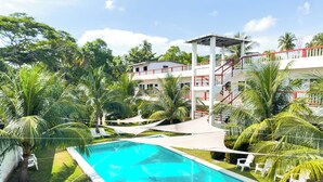 A swimming pool surrounded by palm trees and a white building with red railings. - Hotel Majahual Resort  (La Libertad)