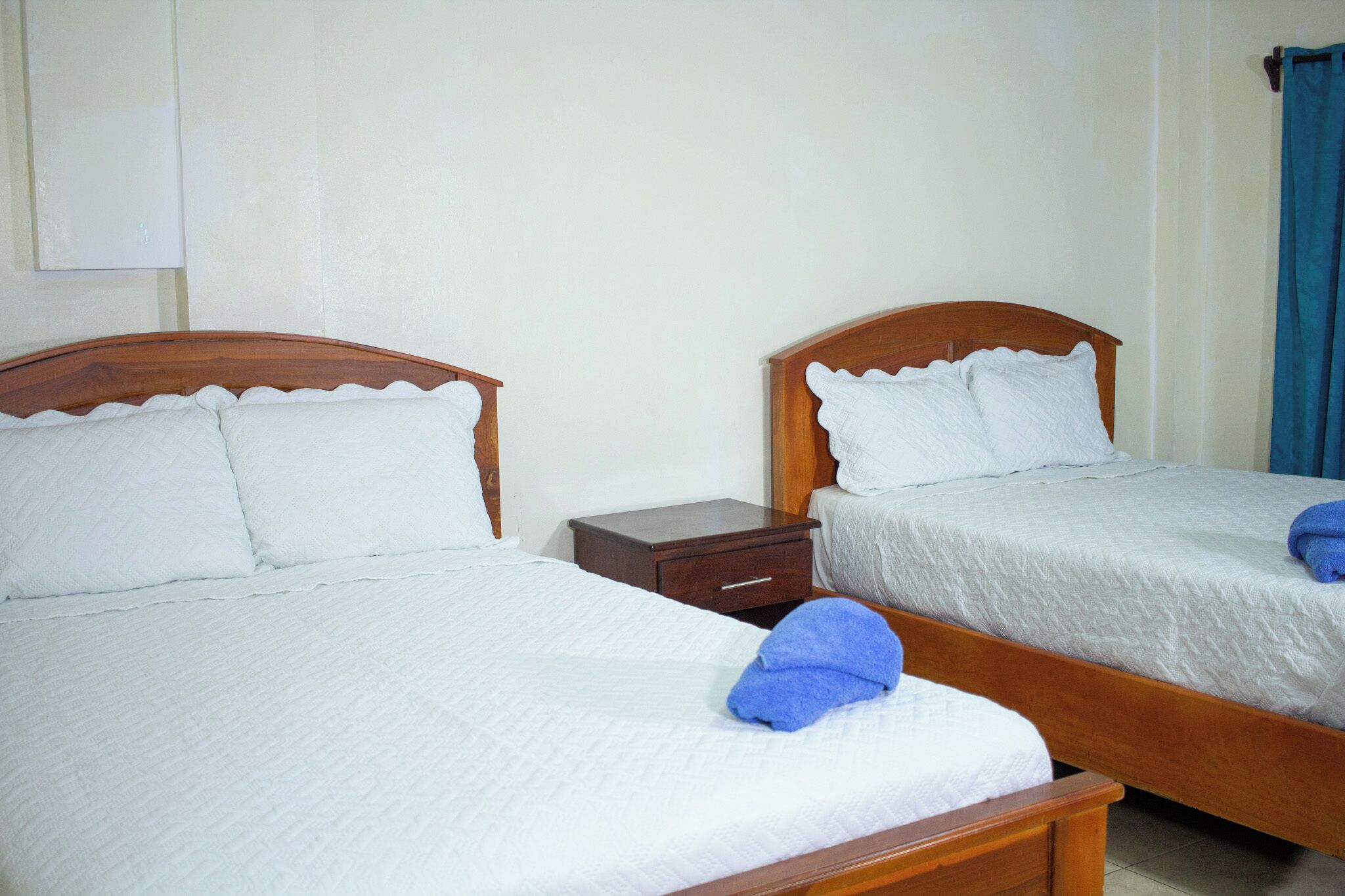 Two single beds with wooden headboards, white linens, and a nightstand between them.