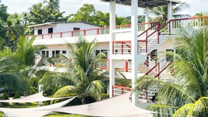 A multi-story building with a red and white exterior, surrounded by palm trees and greenery. - Hotel Majahual Resort  (La Libertad)