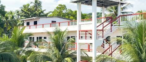 A multi-story building with a red and white exterior, surrounded by palm trees and greenery.