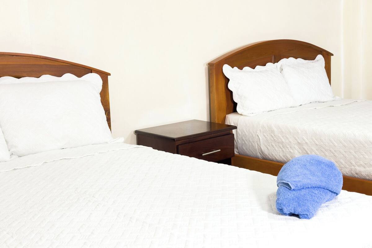 A hotel room with two single beds, a wooden nightstand, and a blue towel on the floor.