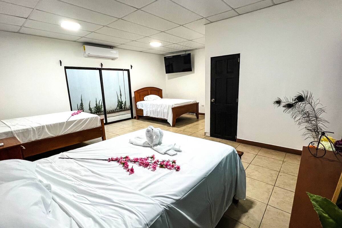 A hotel room with two beds, a television, an air conditioning unit, and a window with a view of trees.
