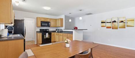 A modern kitchen with wooden cabinets, a dining table, and a refrigerator.
