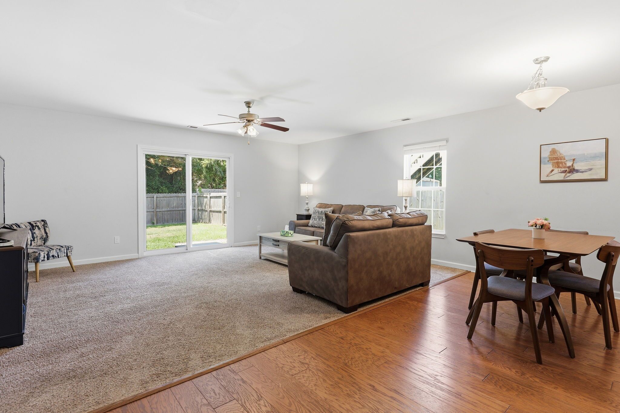 A spacious living room with a large sofa, a dining table with chairs, a ceiling fan, and a sliding glass door leading to a backyard.
