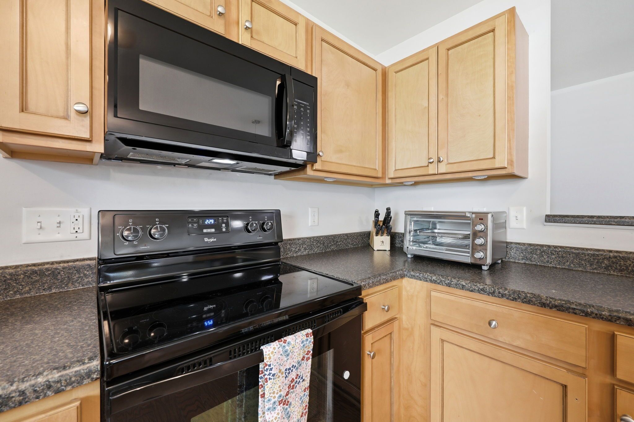 A kitchen with wooden cabinets, a black microwave, a stove, and a toaster.