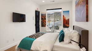 A bedroom with a bed, a TV, a window with a view, and artwork on the walls.