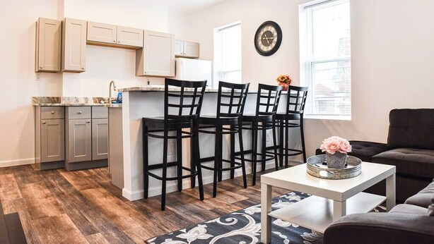 A modern kitchen with a central island, black bar stools, and a dining table with a vase. - Beautiful Pittsburgh home-walkable area w parking (Pittsburgh)