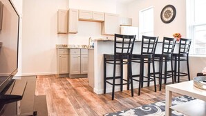 A modern kitchen with light wood cabinets, a central island with bar stools, and a clock on the wall. - Beautiful Pittsburgh home-walkable area w parking (Pittsburgh)