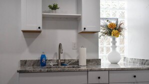 Een keuken met een marmeren aanrecht, een roestvrijstalen spoelbak, een blauwe afwasmiddel-fles, een witte keukenrollenhouder en een vaas met bloemen.