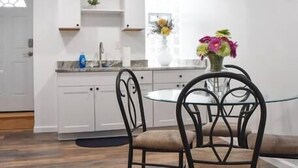Een moderne keuken met witte kasten, een ronde eettafel met twee stoelen en een klok aan de muur.