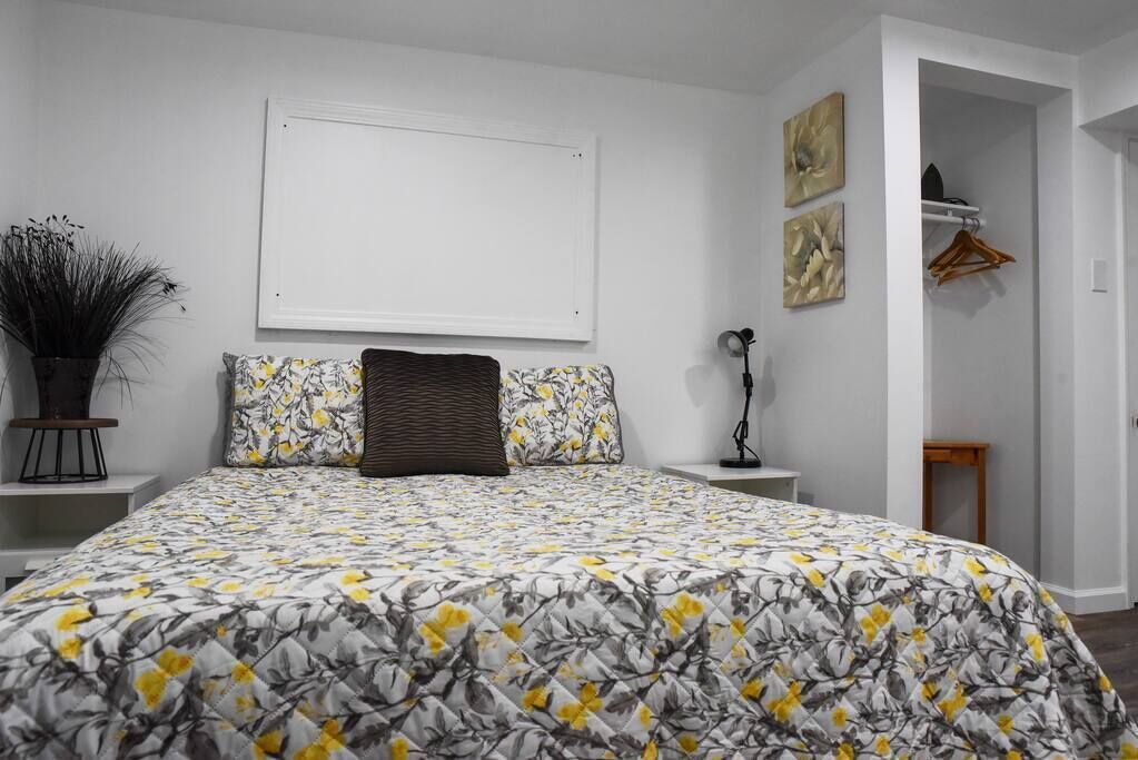 Une chambre à coucher avec une couvre-lit à motifs floraux, une lampe de chevet, une plante en pot et une armoire avec un cintre.
