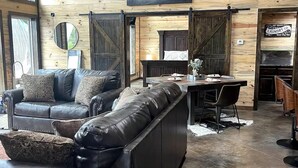 Un interior rústico con un sofá de cuero, una mesa de comedor y un cuadro de un bosque.