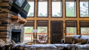 Una sala de estar acogedora con chimenea de piedra, sofá de cuero y un televisor grande montado en la pared.