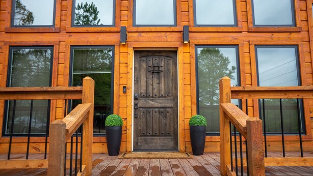 Un edificio de madera con una puerta central, ventanas amplias y una escalera de madera que lleva a una terraza.