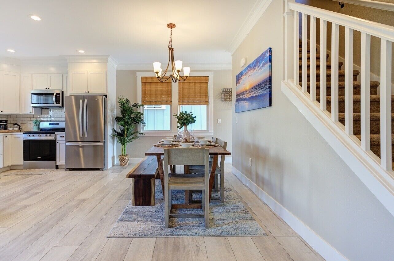 A modern kitchen with stainless steel appliances, a dining area with a wooden table and chairs, and a staircase with white railings.