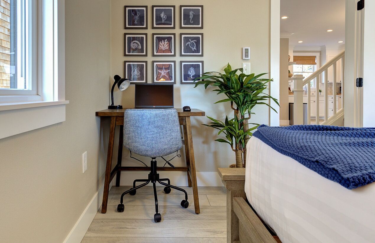 A bedroom with a bed, a desk with a chair, a potted plant, and framed artwork on the wall.