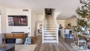 A modern interior with a staircase leading to a kitchen area, a dining table with chairs, and a flat-screen TV mounted on the wall.