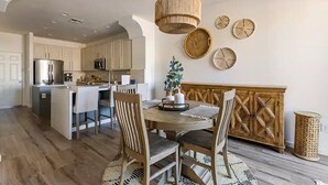 A modern kitchen with a central island, wooden chairs, a round dining table, and a hanging light fixture.