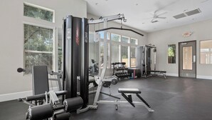 A gym with various exercise equipment, large windows, and a ceiling fan.