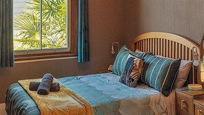 A bedroom with a bed, a chandelier, a window with curtains, a painting, and a nightstand.