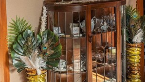A wooden cabinet with glass doors, a round wall clock, and decorative peacock feathers in vases.