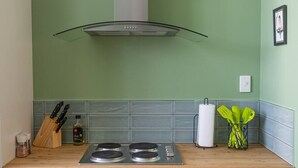 A kitchen with a gas stove, a stainless steel range hood, a wooden countertop, a knife block, a bottle of olive oil, and a paper towel holder.