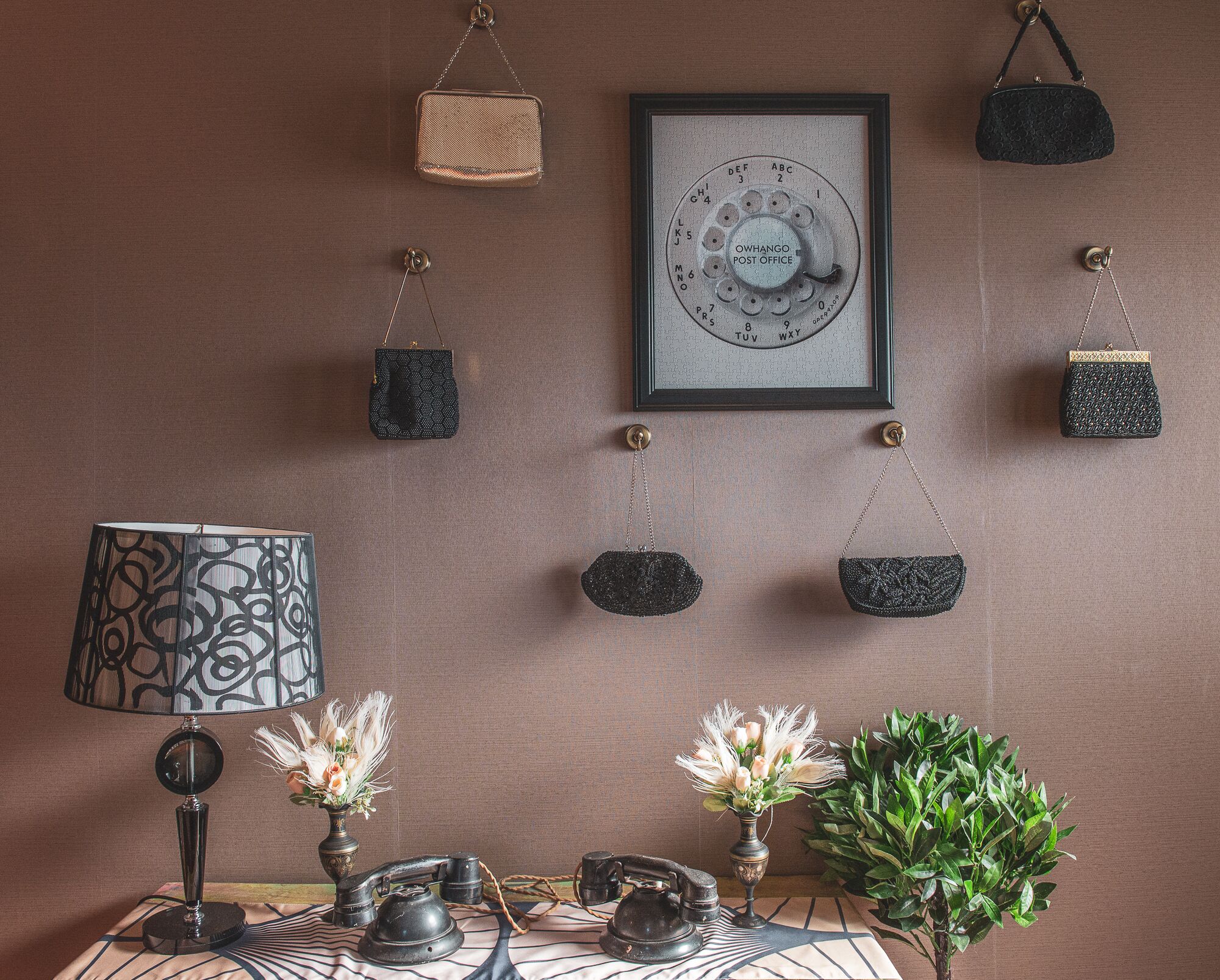 A vintage telephone, a lamp, and several handbags on a wall.