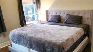 Een slaapkamer met een groot bed, een raam met gordijnen en een bedlampje.