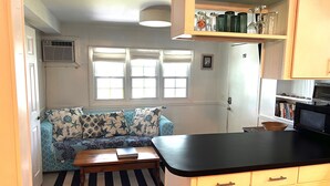 Una cocina compacta con microondas integrado, una mesa de comedor de madera y un sofá con cojines estampados de estrellas.