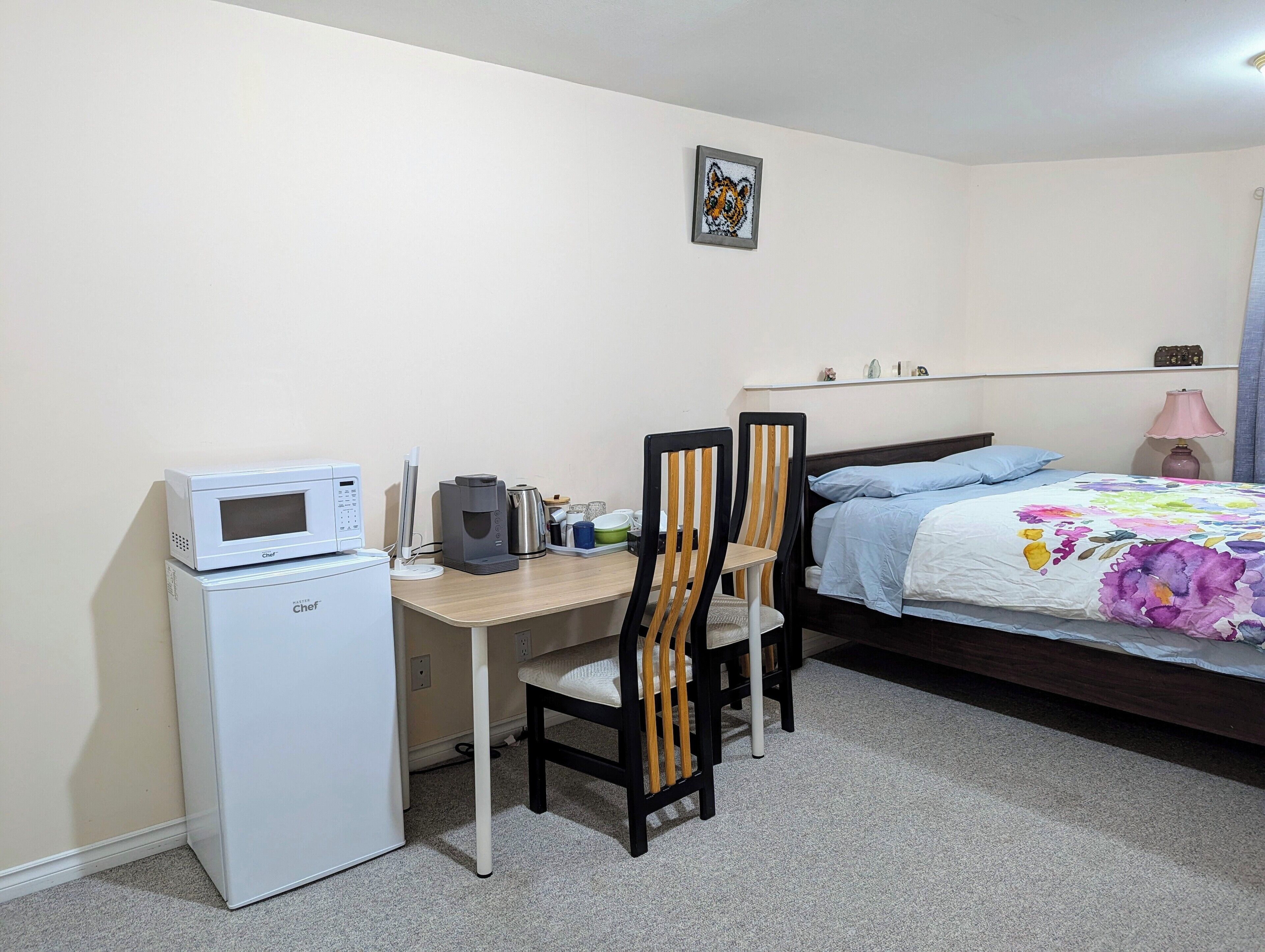 Een slaapkamer met een bed, een bureau met een magnetron, een koffiezetapparaat en twee stoelen.