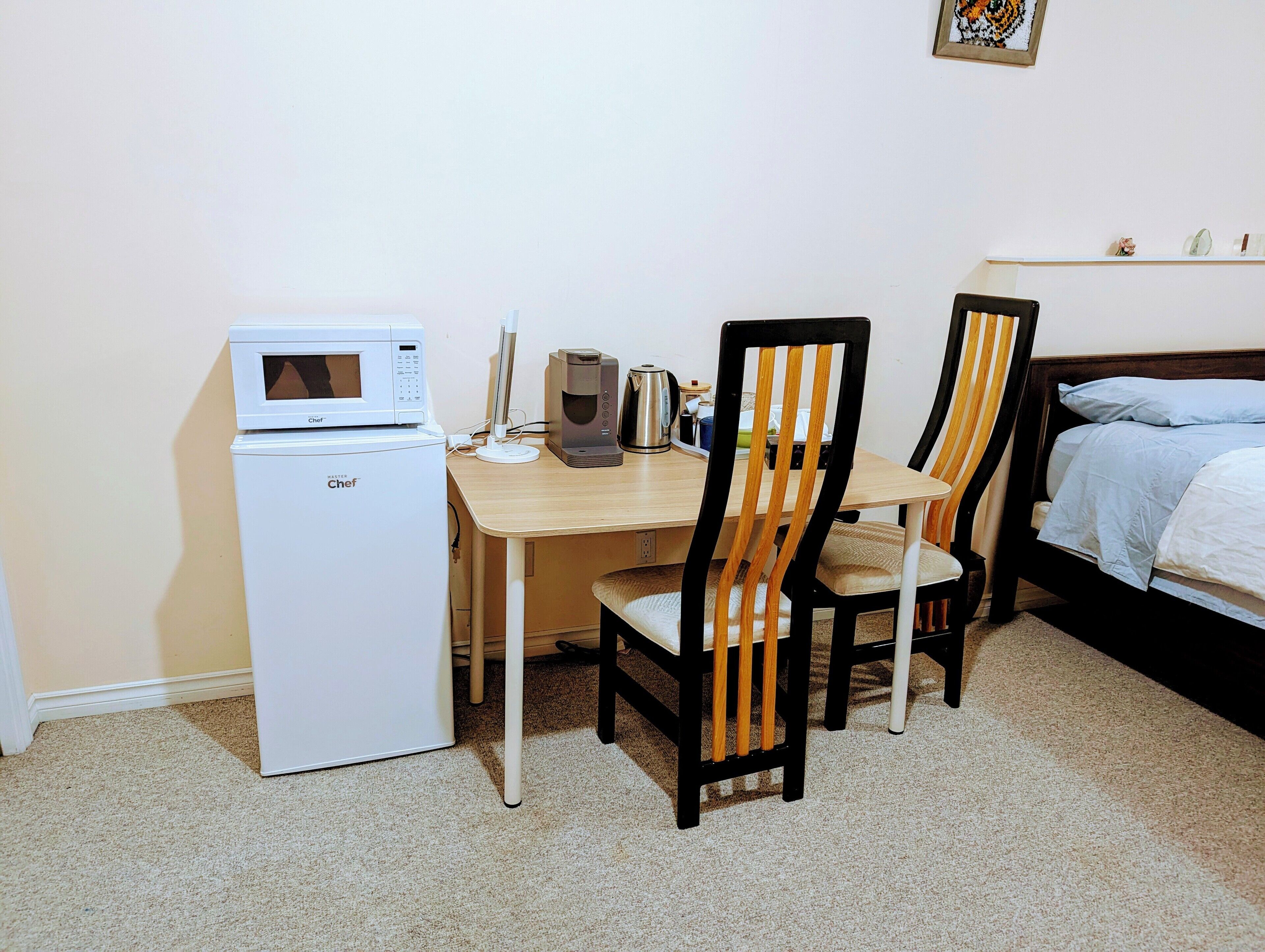 Een compacte kamer met een kitchenette, een houten eettafel, twee stoelen en een bed met een blauwe deken.