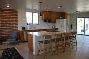 Eine moderne Küche mit einer zentralen Kochinsel, Holzhockern und einer Wand mit Backsteinverkleidung.