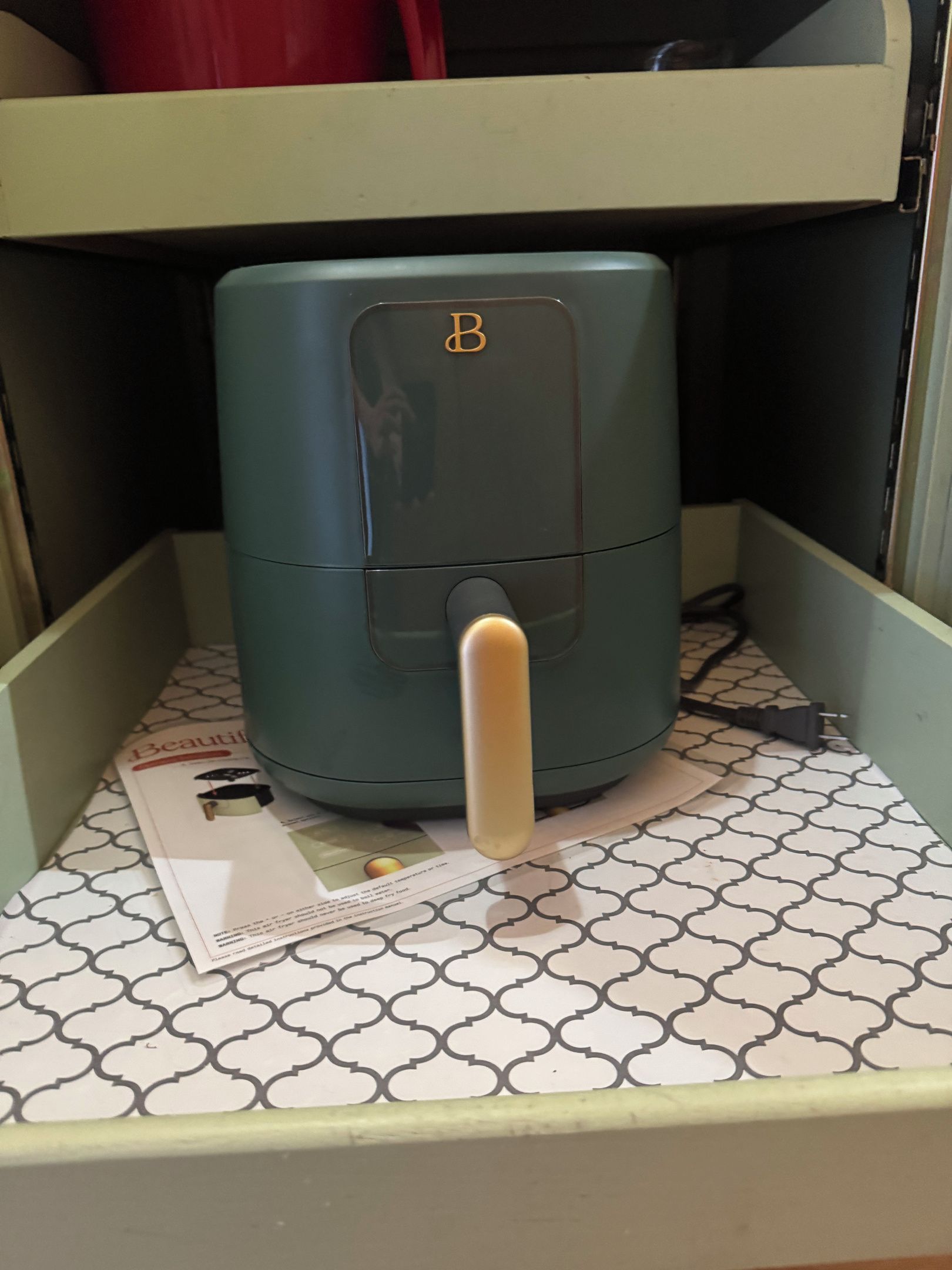 A compact, teal-colored appliance with a control panel and a power cord on a patterned surface.
