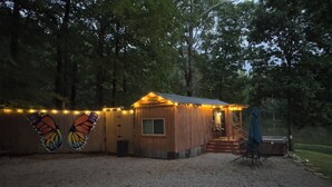 A small wooden cabin with a porch, surrounded by trees, and string lights along the exterior.