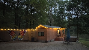 A small wooden cabin with a porch, surrounded by trees, and string lights along the exterior.