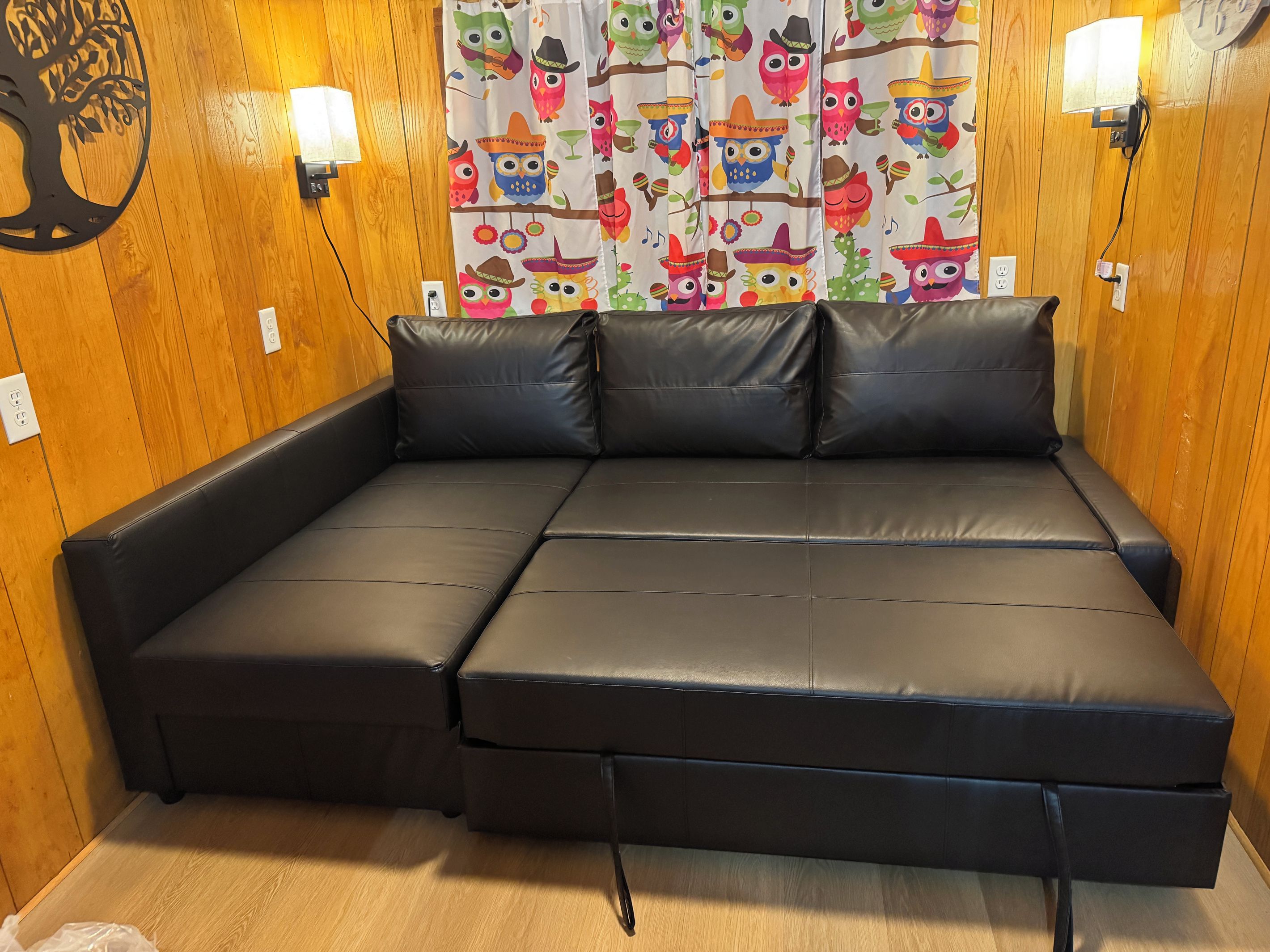 A sectional sofa with a headboard, two wall-mounted lights, and a curtain with colorful owl patterns.