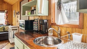 Een keuken met houten wanden, een roestvrijstalen spoelbak, een koffiezetapparaat en een magnetron.